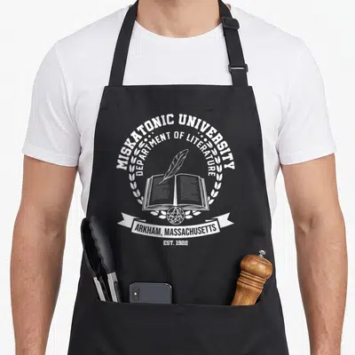 Tablier de cuisine noir avec emblème blanc Université Miskatonic, livre ouvert, plume et mention Arkham Massachusetts Est. 1922.