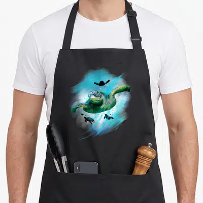 Tablier de cuisine noir avec une tortue de mer peinte dans des tons bleus et verts, entourée de bébés tortues.