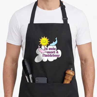 Tablier de cuisine noir avec deux dauphins rose et bleu, un soleil jaune et une bulle de dialogue blanche contenant du texte violet.