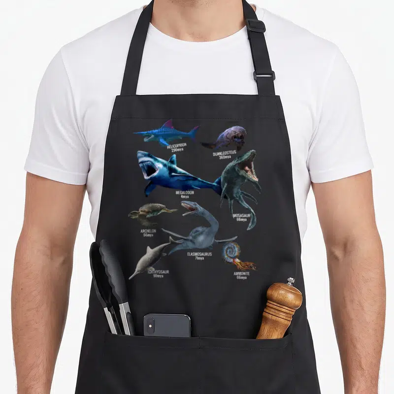 Tablier de cuisine noir avec illustrations de préhistoriques comme le Megalodon et l'Ammonite annotés.