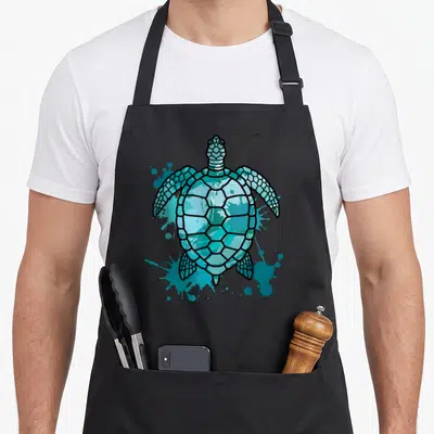 Tablier de cuisine noir avec une illustration de tortue de mer turquoise et des éclaboussures artistiques.