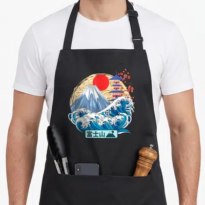 Tablier de cuisine noir avec illustration du Mont Fuji, une grande vague bleue, une pagode et un soleil rouge sur fond beige texturé.