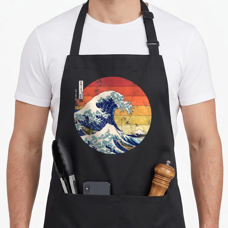 Tablier de cuisine noir avec illustration circulaire De la grande vague de Kanagawa Hokusai sur fond de planches de bois orange et jaune.