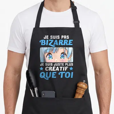 Tablier de cuisine noir avec illustration manga yeux bleus et texte blanc bleu Je suis pas bizarre créatif que toi