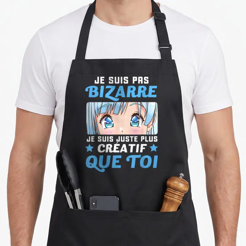 Tablier de cuisine noir avec illustration manga yeux bleus et texte blanc bleu Je suis pas bizarre créatif que toi