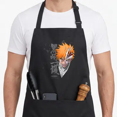 Tablier de cuisine noir avec illustration du visage d'Ichigo aux cheveux orange et masque blanc caractéristique.