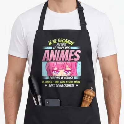 Tablier de cuisine noir avec une fille aux cheveux roses et le texte Je ne regarde pas tout le temps des animes imprimé en lettres colorées.