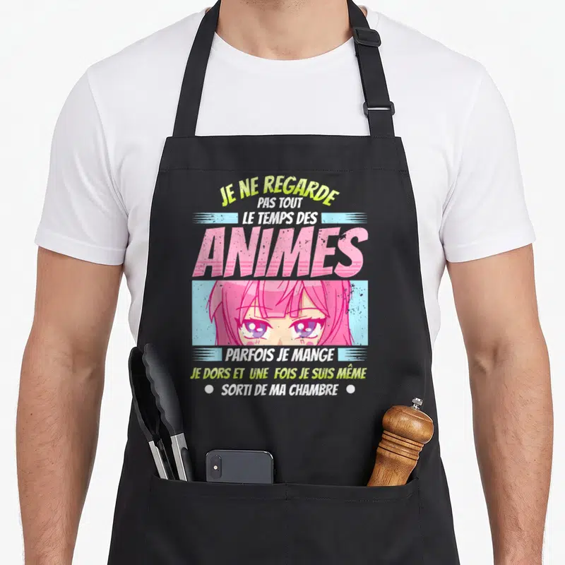 Tablier de cuisine noir avec une fille aux cheveux roses et le texte Je ne regarde pas tout le temps des animes imprimé en lettres colorées.