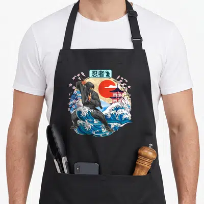 Tablier de cuisine noir avec illustration ninja sur vague bleue, soleil rouge et fleurs de sakura dans un style japonais vintage.