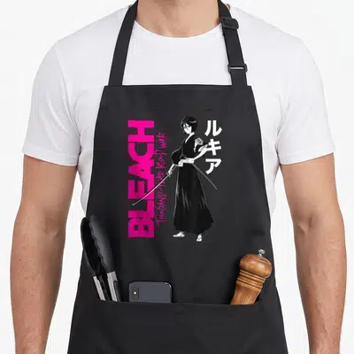 Tablier de cuisine noir avec illustration de Rukia, texte BLEACH rose et caractères japonais blancs sur fond uni.