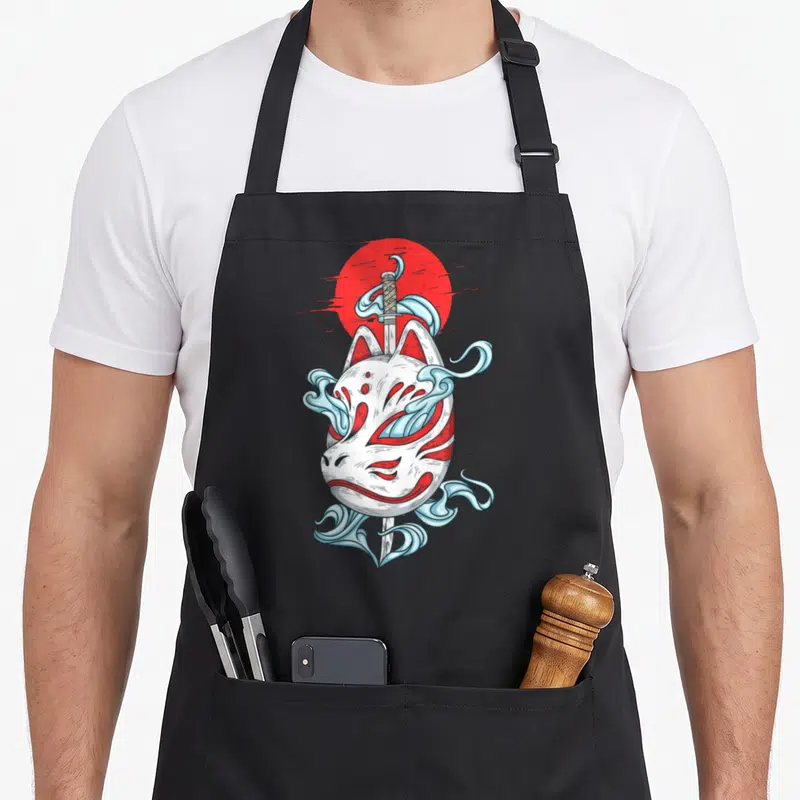 Tablier de cuisine noir avec masque blanc kitsune, katana et nuages bleus sur fond de soleil rouge.