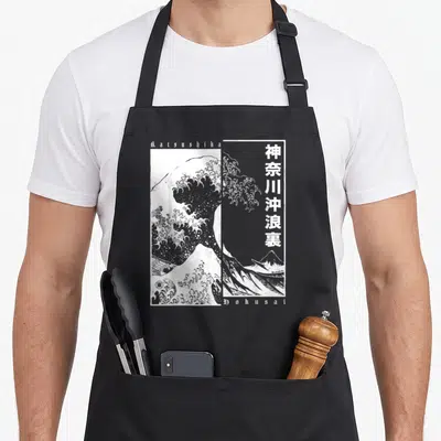 Tablier de cuisine noir avec une reproduction monochrome de la Grande Vague de Kanagawa et des caractères japonais verticaux.