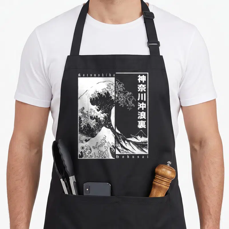 Tablier de cuisine noir avec une reproduction monochrome de la Grande Vague de Kanagawa et des caractères japonais verticaux.