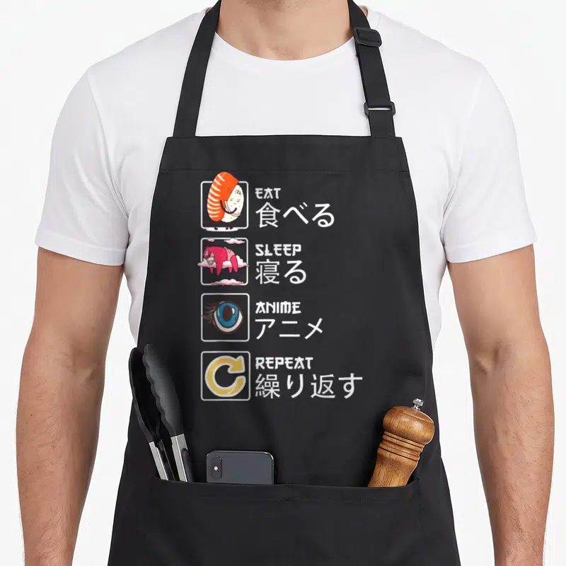Tablier de cuisine noir avec illustrations manga Eat Sleep Anime Repeat et caractères japonais en blanc sur fond sombre.