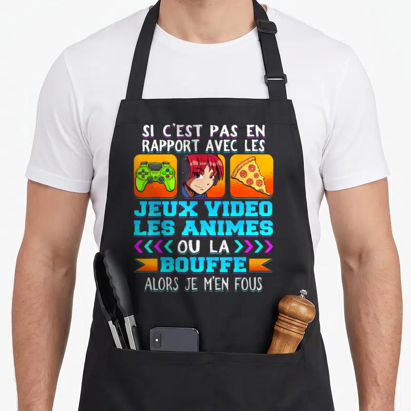 Tablier de cuisine noir avec une illustration de fille aux cheveux roses, manette verte et pizza sous un slogan humoristique sur les passions.