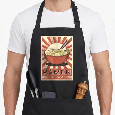 Tablier de cuisine noir avec illustration rétro d'un bol de ramen aux baguettes et texte RAMEN en bas.