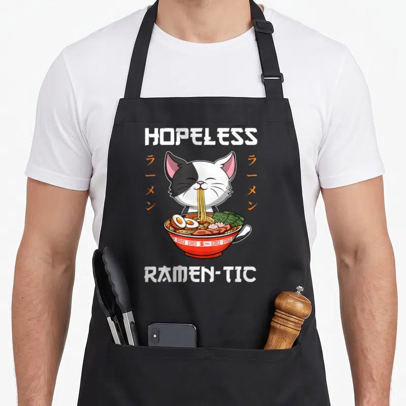 Tablier de cuisine noir avec illustration d'un chat mangeant du ramen et le texte Hopeless Ramen-tic.