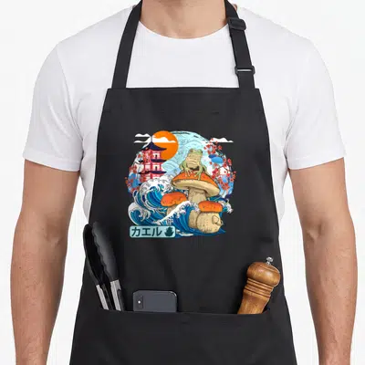 Tablier de cuisine noir avec illustration d'une grenouille sur un champignon face à une grande vague japonaise.