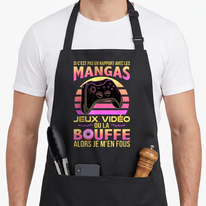 Tablier de cuisine noir avec illustration de manette de jeu et texte coloré sur les mangas et la bouffe.