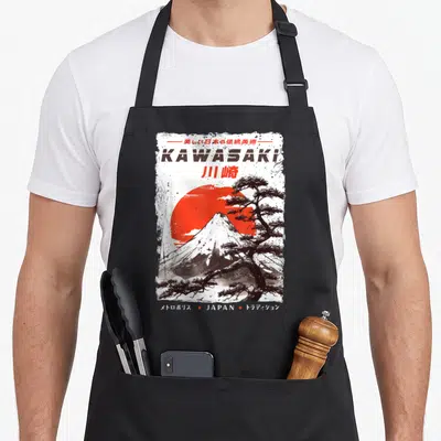 Tablier de cuisine noir avec illustration Kawasaki rouge et arbre stylisé noir sur fond blanc texturé.
