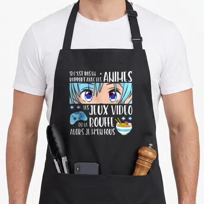 Tablier de cuisine noir avec illustration de yeux anime bleus, manette de jeu vidéo et bol de ramen sous un slogan humoristique.