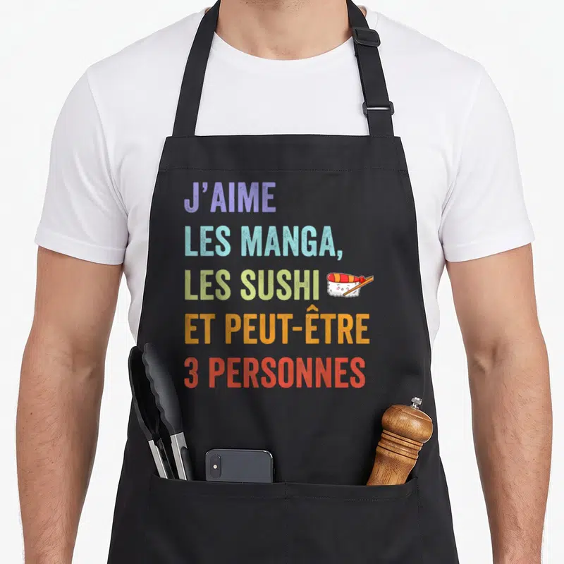 Tablier de cuisine noir avec texte coloré J'aime les manga les sushi et peut-être 3 personnes accompagné d'une illustration de sushi souriant.