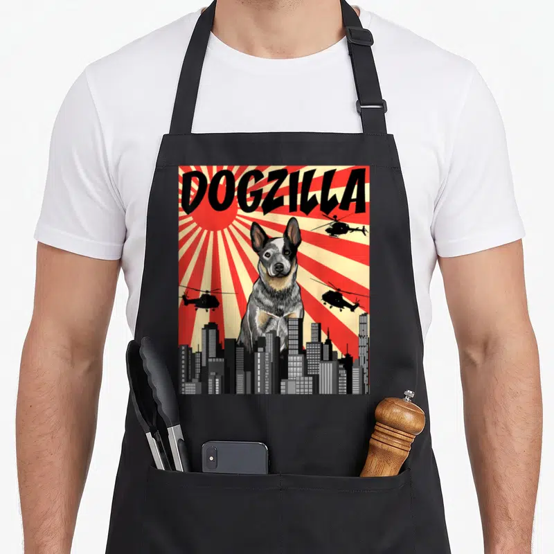 Tablier de cuisine noir avec illustration d'un chien géant type kaiju sur fond de soleil rayonnant rouge et ville grise.