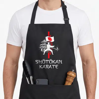 Tablier de cuisine noir avec silhouette de karatéiste, pagode et texte Shōtōkan Karate en blanc et rouge.
