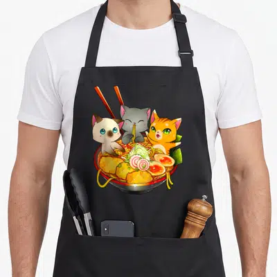 Tablier de cuisine noir avec trois chats kawaii autour d'un bol de ramen coloré et appétissant.