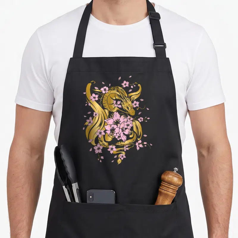 Tablier de cuisine noir avec un dragon doré et des fleurs de cerisier sakura roses imprimés au centre.