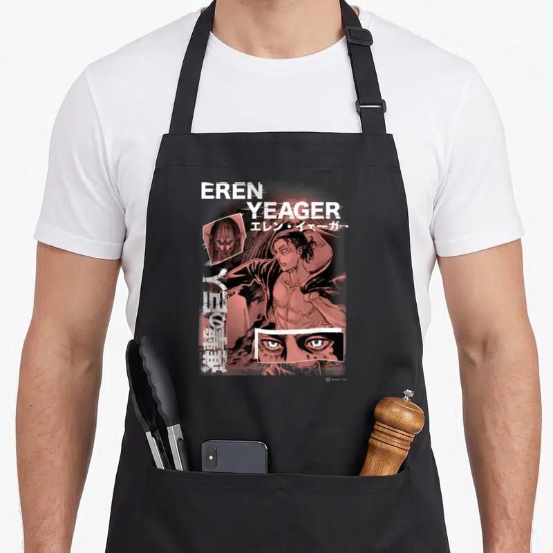 Tablier de cuisine noir avec collage d'Eren Yeager, yeux détaillés et texte japonais en blanc et rouge.