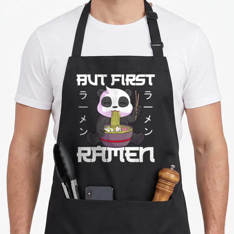 Tablier de cuisine noir avec un panda kawaii mangeant du ramen et le texte But First Ramen.