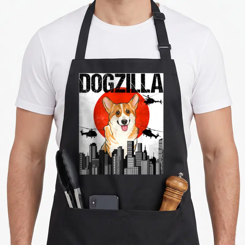 Tablier de cuisine noir avec un corgi géant surnommé Dogzilla dominant une ville sous un soleil rouge japonais.