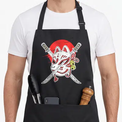 Tablier de cuisine noir avec un masque kitsune blanc, deux sabres samouraï croisés et des clochettes dorées devant un soleil rouge.