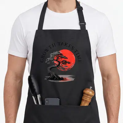 Tablier de cuisine noir avec un bonsaï stylisé devant un grand disque solaire rouge vif.