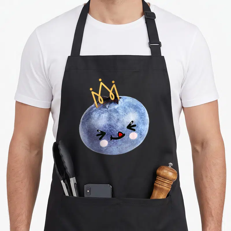Tablier de cuisine noir avec une myrtille princesse kawaii coiffée d'une couronne dorée et un visage souriant.
