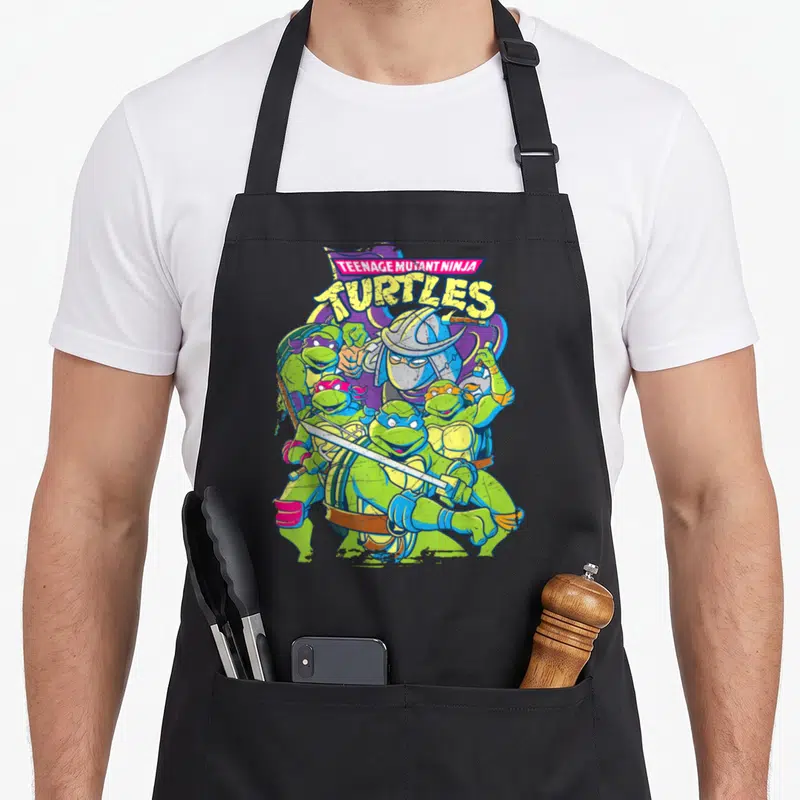 Tablier de cuisine noir avec illustration des Tortues Ninja et Shredder en position de combat sous le logo Teenage Mutant Ninja Turtles.