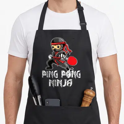 Tablier de cuisine noir avec illustration d'un Ping Pong Ninjatenant une raquette rouge et le texte PING PONG NINJA en blanc.