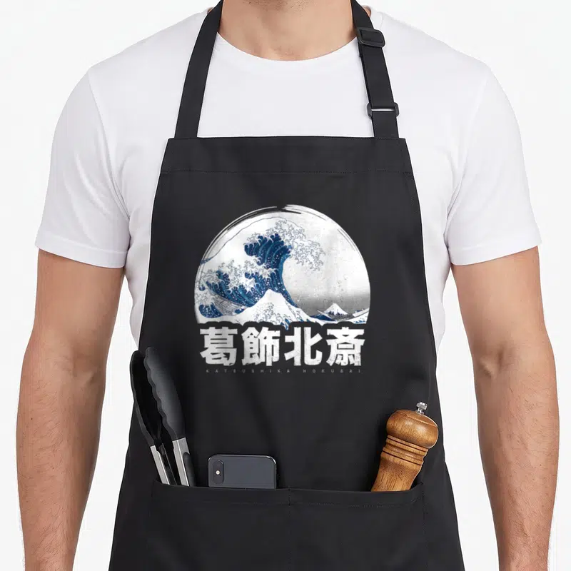 Tablier de cuisine noir avec une grande vague bleue et des caractères japonais blancs imprimés au centre.