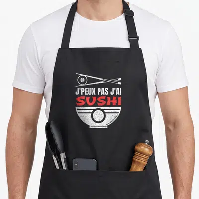 Tablier de cuisine noir avec un bol blanc, des baguettes croisées et le texte J'peux pas j'ai Sushi en rouge et blanc.