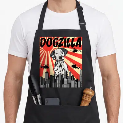Tablier de cuisine noir avec illustration Dogzilla dalmatien géant sur fond de ville et hélicoptères sous un soleil rayonnant.