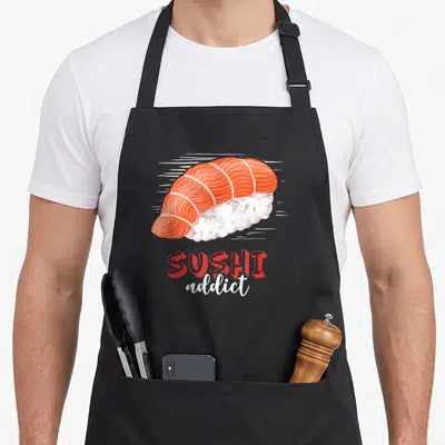 Tablier de cuisine noir avec illustration colorée d'un sashimi de saumon et du texte Sushi addict en rouge et blanc.