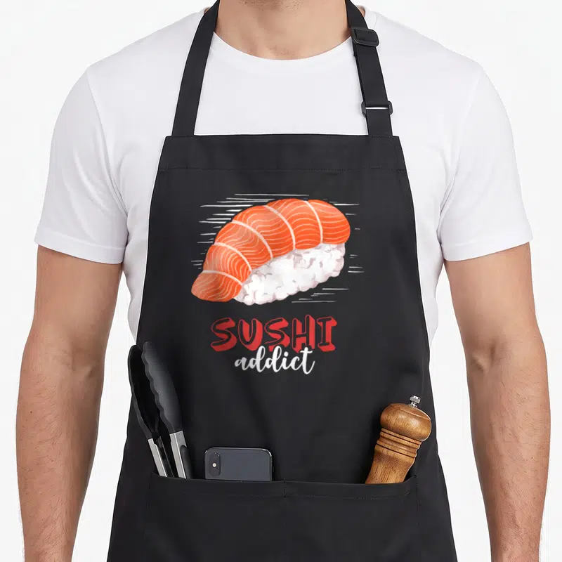 Tablier de cuisine noir avec illustration colorée d'un sashimi de saumon et du texte Sushi addict en rouge et blanc.