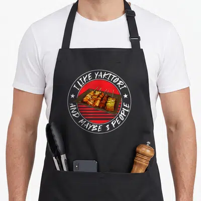 Tablier de cuisine noir avec illustration circulaire de brochettes Yakitori sur fond rouge rayé et texte blanc.