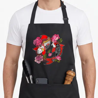 Tablier de cuisine noir avec deux carpes Nishikigoi rouges et noires entourées de fleurs de pivoine roses et vertes dans un style kawaii japonais.