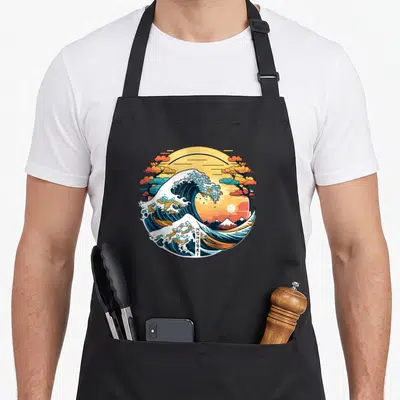 Tablier de cuisine noir avec une illustration circulaire d'un tsunami stylisé Manga et du Mont Fuji au fond.