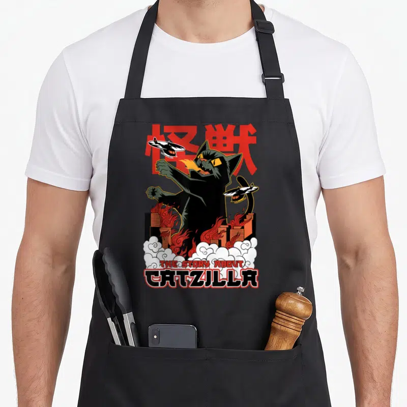 Tablier de cuisine noir avec illustration d'un chat monstre crachant du feu et des hélicoptères.