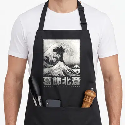 Tablier de cuisine noir avec reproduction en noir et blanc de La Grande Vague de Kanagawa et la signature de l'artiste en bas.