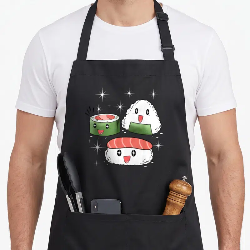 Tablier de cuisine noir avec trois pièces de sushi kawaii aux visages souriants et des étoiles scintillantes autour.