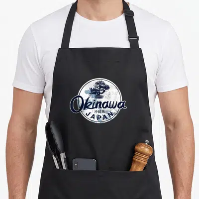 Tablier de cuisine noir avec logo circulaire Okinawa Japon et illustration de bonsaï bleu marine.
